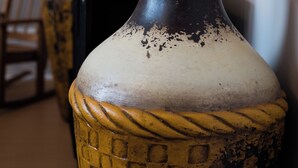 A close-up of a decorative vase with a textured pattern, placed on a table with a candle and a gramophone in the background.