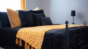 A bed with a black frame, a yellow patterned blanket, and several pillows in black and yellow.
