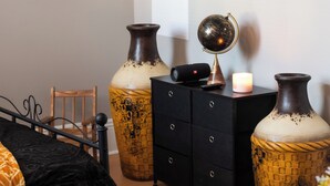 A bedroom with a bed, a dresser, two large vases, a globe, and a lit candle.