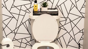 A bathroom with a geometric-patterned wall, a toilet, a trash can, and a toilet brush.