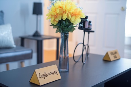 A room with a table featuring a vase of yellow flowers, a name card, and a small table with a name card.
