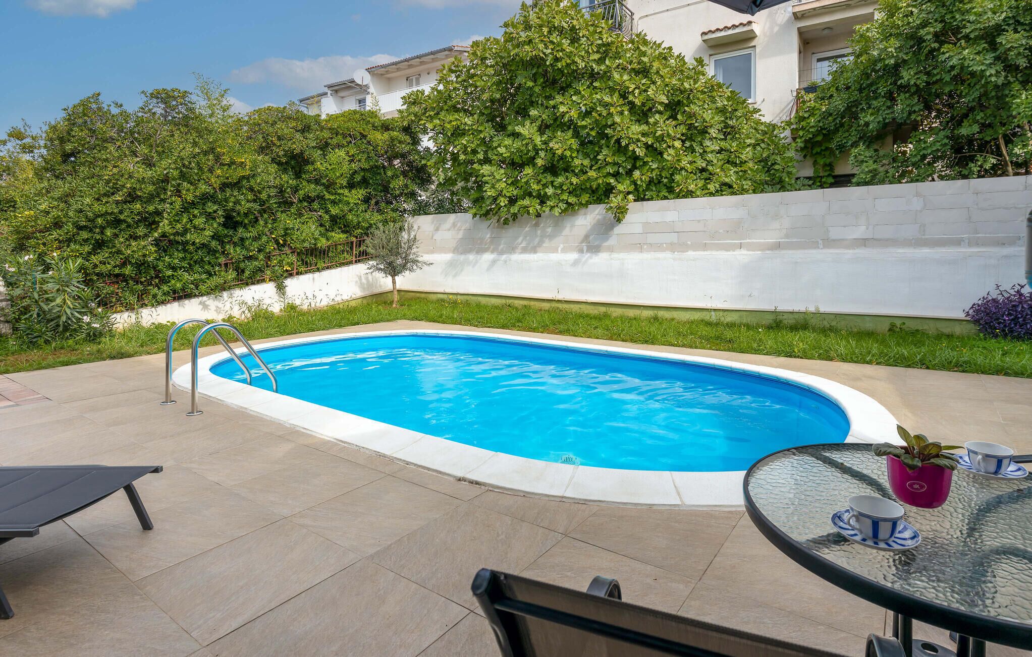 A swimming pool with a metal ladder, surrounded by a white wall and greenery.