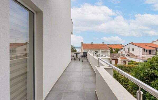 A balcony with a table and chairs, overlooking a residential area with red-tiled roofs.