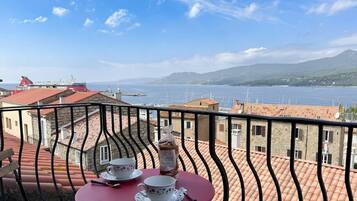 Ein Balkon mit gedecktem Tisch für zwei Personen, mit Blick auf einen Hafen, Boote und eine ferne Bergkette.