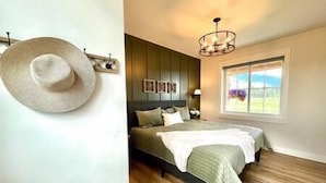 A bedroom with a bed, a wall-mounted hat, and a window with a view. - Luxe 1br Cottage - Mtn Views! "Cedar" (Columbia Falls)
