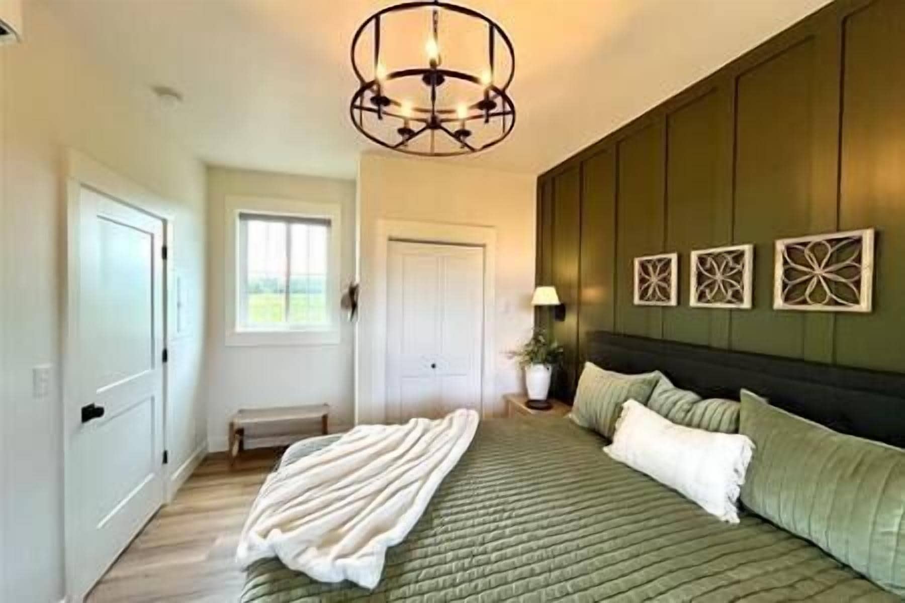 A bedroom with a green bedspread, a white throw blanket, and a decorative ceiling light.