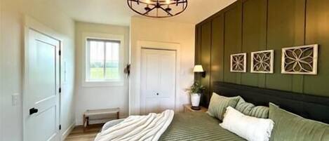 A bedroom with a green bedspread, a white throw blanket, and a decorative ceiling light.
