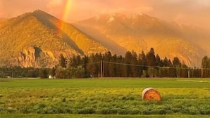 A mountain landscape with a rainbow, a hay bale, and a field. - Luxe 1br Cottage - Mtn Views! "Cedar" (Columbia Falls)