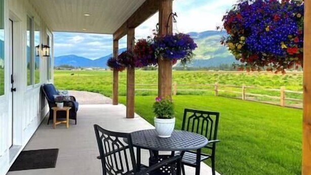 A covered outdoor seating area with a table and chairs, a potted plant, and hanging flower baskets. - Luxe 1br Cottage - Mtn Views! "Cedar" (Columbia Falls)
