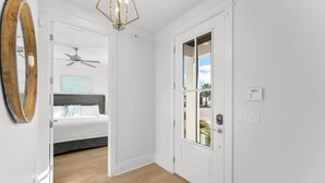 Un pasillo con piso de madera, una puerta blanca con panel de vidrio, un ventilador de techo y una lámpara fijada a la pared.