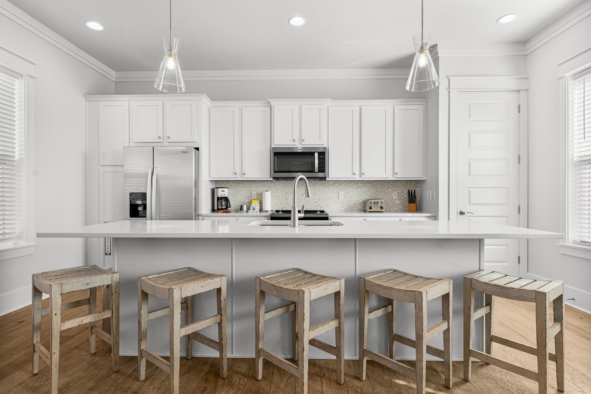A modern kitchen with white cabinetry, a central island with stools, stainless steel appliances, and pendant lighting.