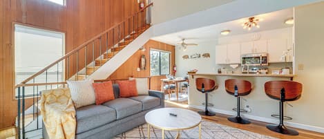 A spacious living area with a gray sofa, a coffee table, and a staircase leading to an upper level.