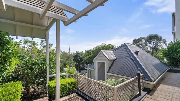 A covered outdoor area with a wooden deck, a small shed, and a view of a city skyline in the background. - Parnell Self-Contained Cottage

 (Auckland)