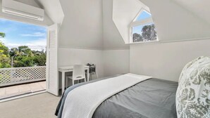 A bedroom with a bed, a desk, and a window overlooking greenery. - Parnell Self-Contained Cottage

 (Auckland)