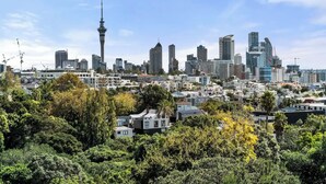 A cityscape with modern high-rise buildings, a prominent tower, and dense greenery in the foreground. - Parnell Self-Contained Cottage

 (Auckland)