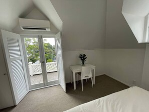 A bedroom with a bed, a small table with a chair, and a balcony door leading to an outdoor area. - Parnell Self-Contained Cottage
(Auckland)