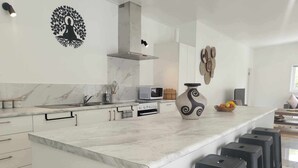 A modern kitchen with a marble countertop, a built-in oven, and a large island with bar stools.