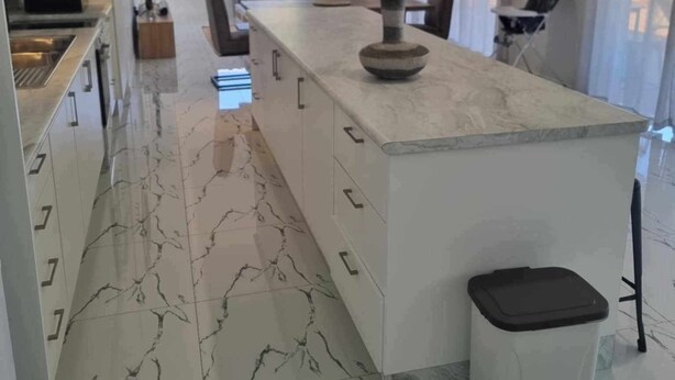 A modern kitchen with a marble countertop, a central island, and a dining area with a sofa and chairs.