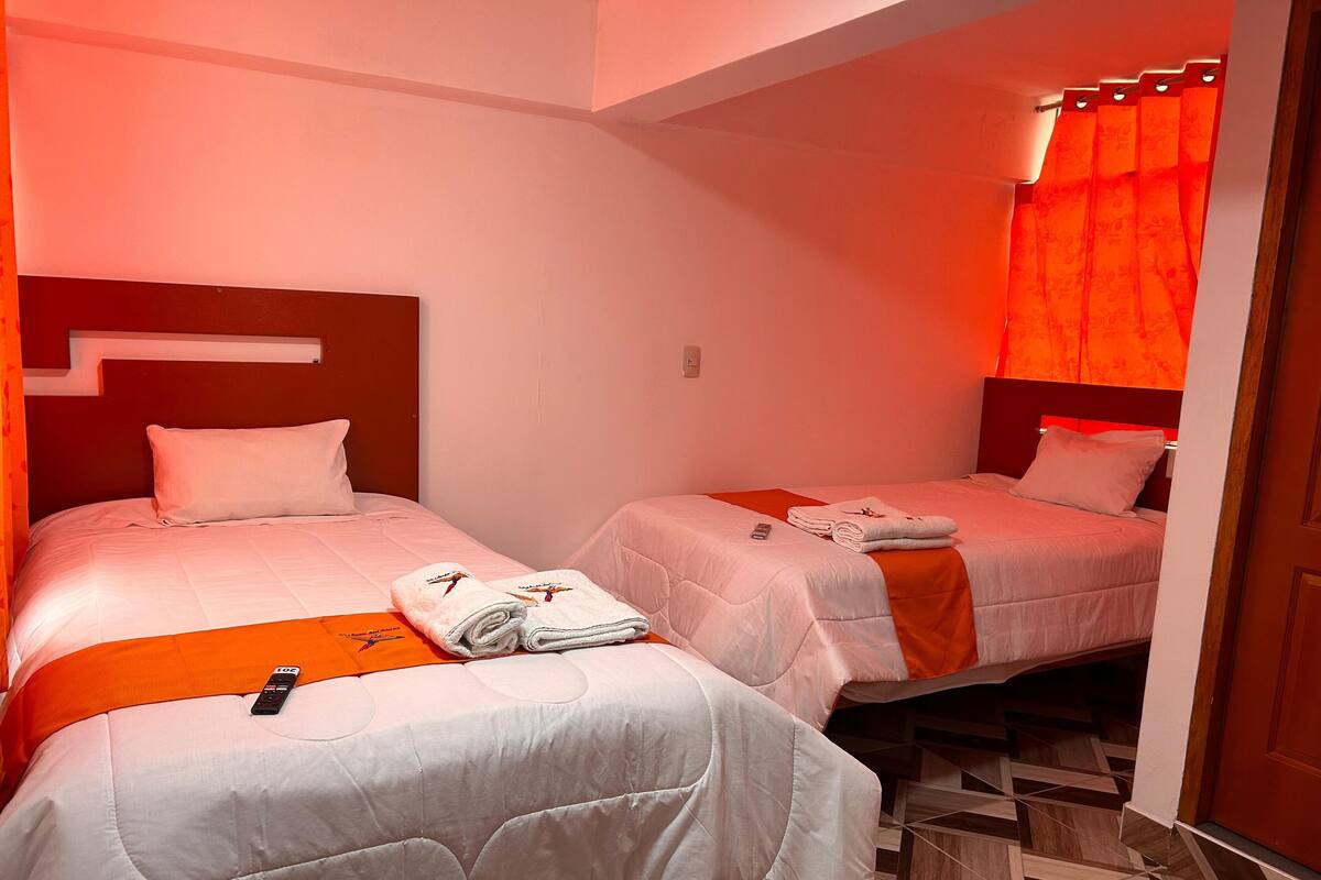Habitación de hotel con dos camas, cada una con un edredón blanco y almohadas, y una pared de acento en color rojo.