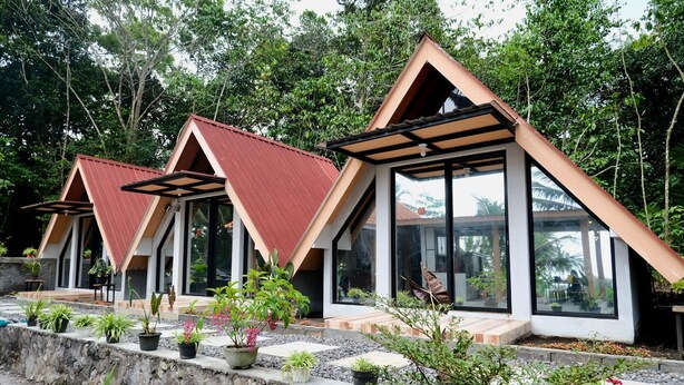 Une rangée de cabanes modernes, dotées de toits triangulaires et de grandes fenêtres, entourées d’une végétation luxuriante et de plantes en pot.