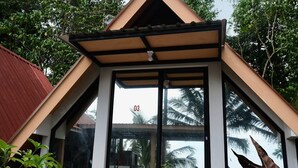 Une maison moderne avec un toit triangulaire, de grandes fenêtres en verre et un chemin de pierre menant à l’entrée.