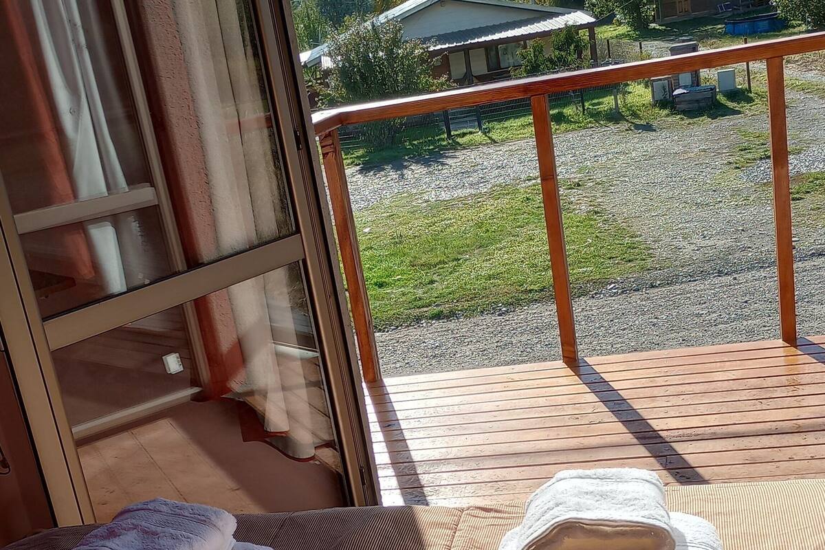 Un balcón con barandilla de madera, vista a un área verde y dos toallas apiladas sobre un cojín a rayas.