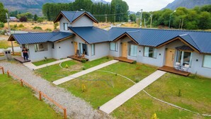 A modern two-story building with a covered patio area, a gravel driveway, and a well-maintained lawn. - cabañas del sauce (El Hoyo)