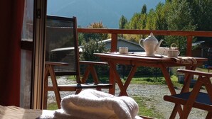 A room with a wooden table set for tea, a window overlooking mountains, and a bed with a white blanket. - cabañas del sauce (El Hoyo)