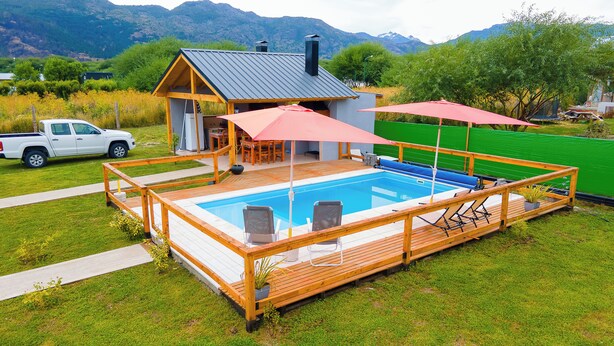 A swimming pool with a wooden deck, a small building with a sloped roof, and a white pickup truck parked nearby. - cabañas del sauce (El Hoyo)