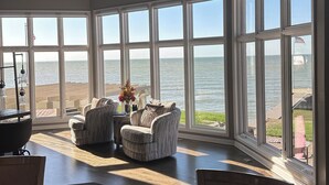 A spacious room with large windows overlooking a body of water, furnished with a sofa, chairs, and a dining table.