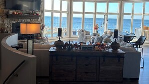 A spacious living area with a stone fireplace, a large flat-screen TV, and a view of the ocean through large windows.
