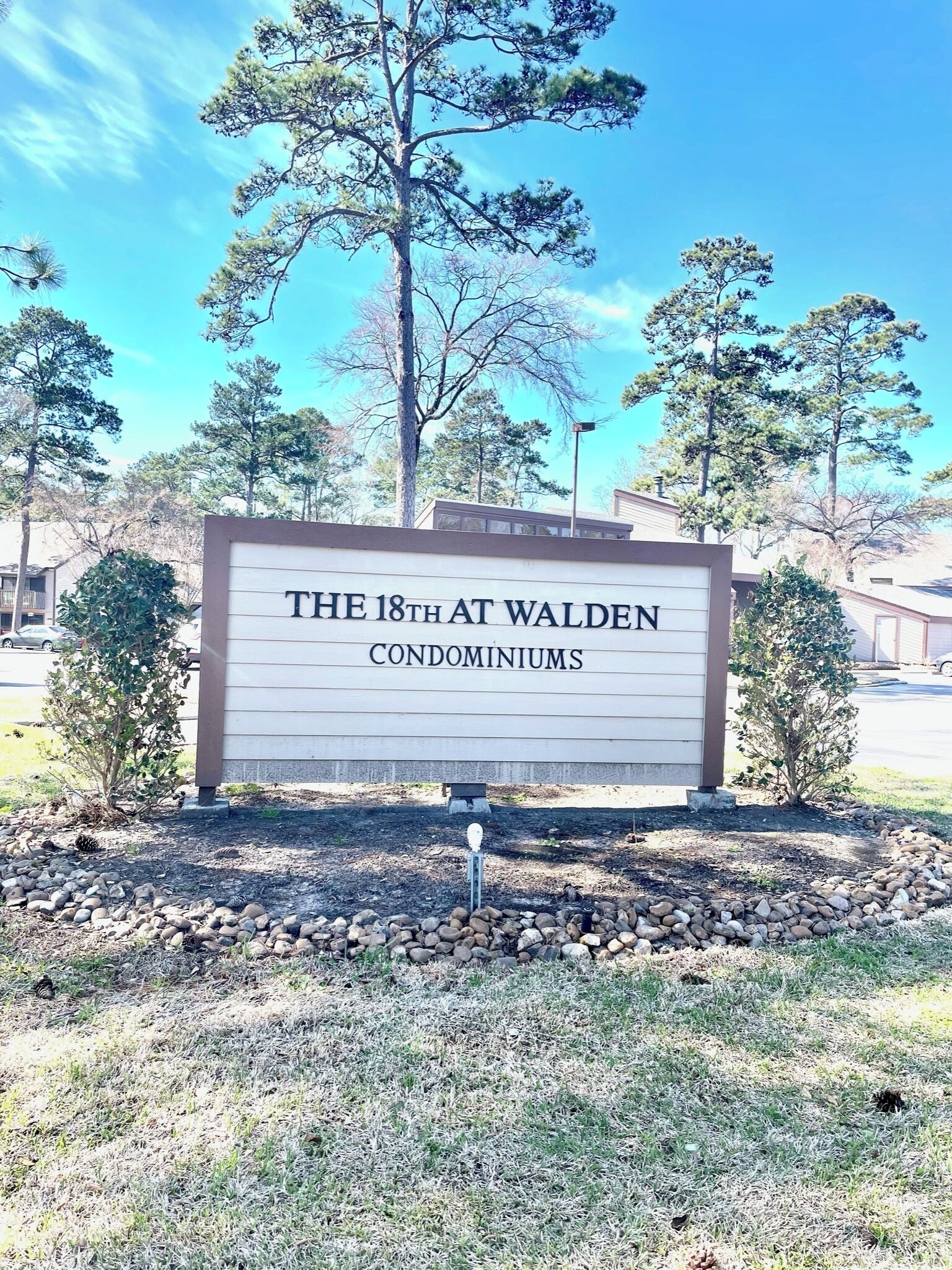 A sign for 'The 18th at Walden Condominiums' with a clear sky and trees in the background.