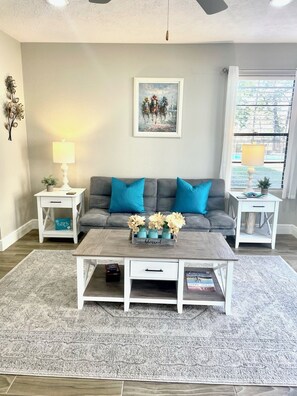 A living room with a grey sofa, two side tables, a coffee table, and a painting on the wall.