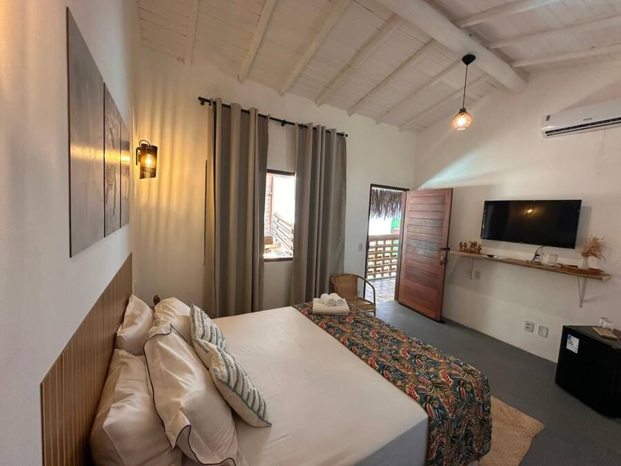 Una habitación de hotel con cama, televisor, ventana con cortinas y techo de madera.