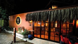 A building with a thatched roof, a sign with a tree logo, and a red vehicle parked outside. - AROEIRA POUSADA TRANCOSO (Porto Seguro)