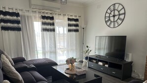 A modern living room with a black sofa, a glass coffee table, a TV, and a decorative clock on the wall. - 3 Bedroom cozy villa in Werribee near  Werribee CBD and other amenities (Werribee)