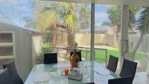 A glass-top dining table with chairs, a vase, and a clock. - 3 Bedroom cozy villa in Werribee near  Werribee CBD and other amenities (Werribee)