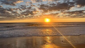 A beach scene with the sun setting over the ocean, creating a calm atmosphere.