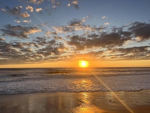 A beach scene with the sun setting over the ocean, creating a calm atmosphere.