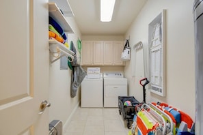 A laundry room with a washing machine, dryer, and a cart with colorful bags.