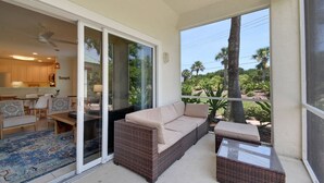 A balcony with a wicker sofa, a glass-top table, and a view of a tropical landscape.