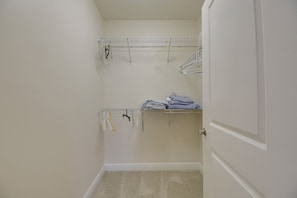 A small, enclosed closet with a metal shelving unit and a hanging rod, containing folded clothes and a pair of scissors.