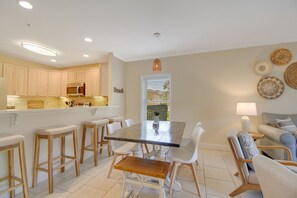 A modern kitchen with white cabinets, a dining table with white chairs, and a bar area with stools. - Ocean Reef 101 - Ocean Bliss (St Augustine Beach)