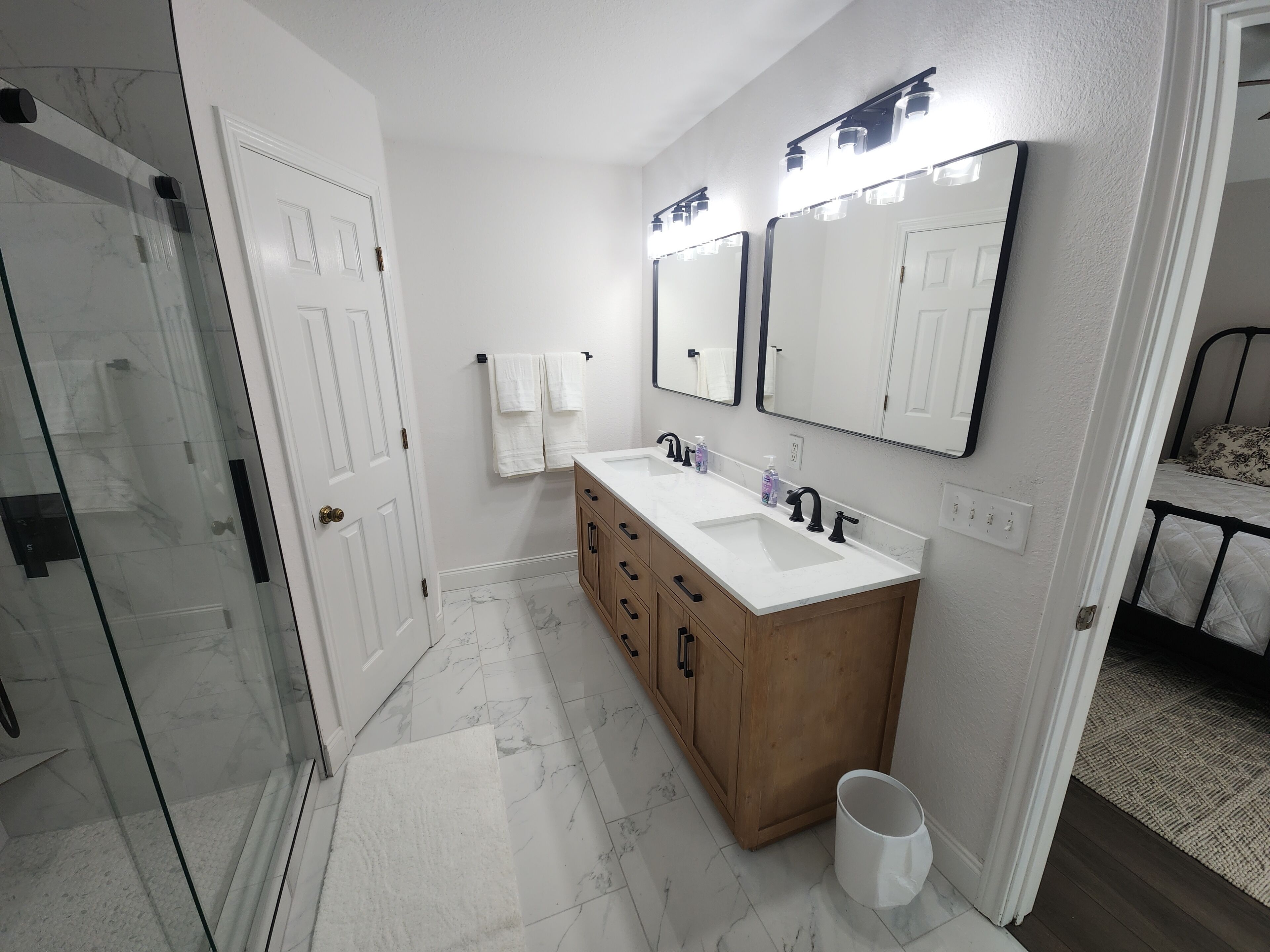 Une salle de bain moderne avec un meuble-lavabo blanc, une douche en verre et un lit dans la pièce adjacente.