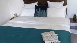 Un lit bien fait, avec une literie blanche et turquoise, un plaid à motifs et un tableau accroché au mur au-dessus.