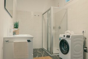 Un bagno con cabina doccia in vetro, lavatrice e porta asciugamani.