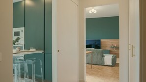 A modern kitchen with teal cabinets, a microwave, and a dining area with clear glass stools. - Rafael Green Home - MyHomeinComo (Como)