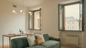 A modern living room with a sofa, a dining table, and a large window. - Rafael Green Home - MyHomeinComo (Como)