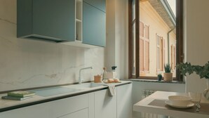 A modern kitchen with a marble countertop, white cabinets, and a window with shutters. - Rafael Green Home - MyHomeinComo (Como)