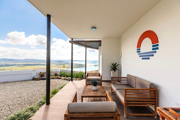 A covered outdoor seating area with a view of a mountainous landscape and a pool.
